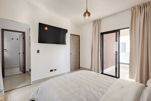 Een moderne slaapkamer met een groot bed, een flatscreen televisie aan de muur en een schuifdeur naar een buitenruimte.