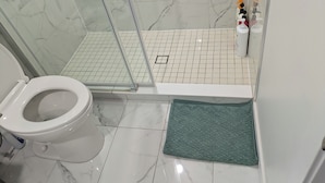 Ein Badezimmer mit Toilette, einer Duschkabine mit Glastür und Fliesenboden.