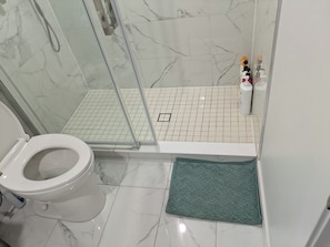 A bathroom with a toilet, a shower area with a glass door, and a tiled floor. - 3 Bedroom Modern, Stylish & Spacious Home with King Size Bed! (Stratford)