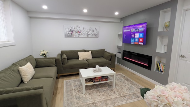 Ein modernes Wohnzimmer mit einer Eckcouch, einem Flachbildfernseher an der Wand, einem Kamin und einem Couchtisch mit Büchern.