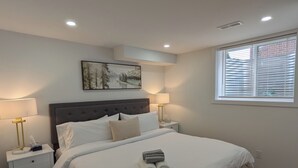 Ein Schlafzimmer mit einem großen Bett, zwei Nachttischen mit Lampen, einem Fenster mit Jalousien und einem Bild an der Wand.