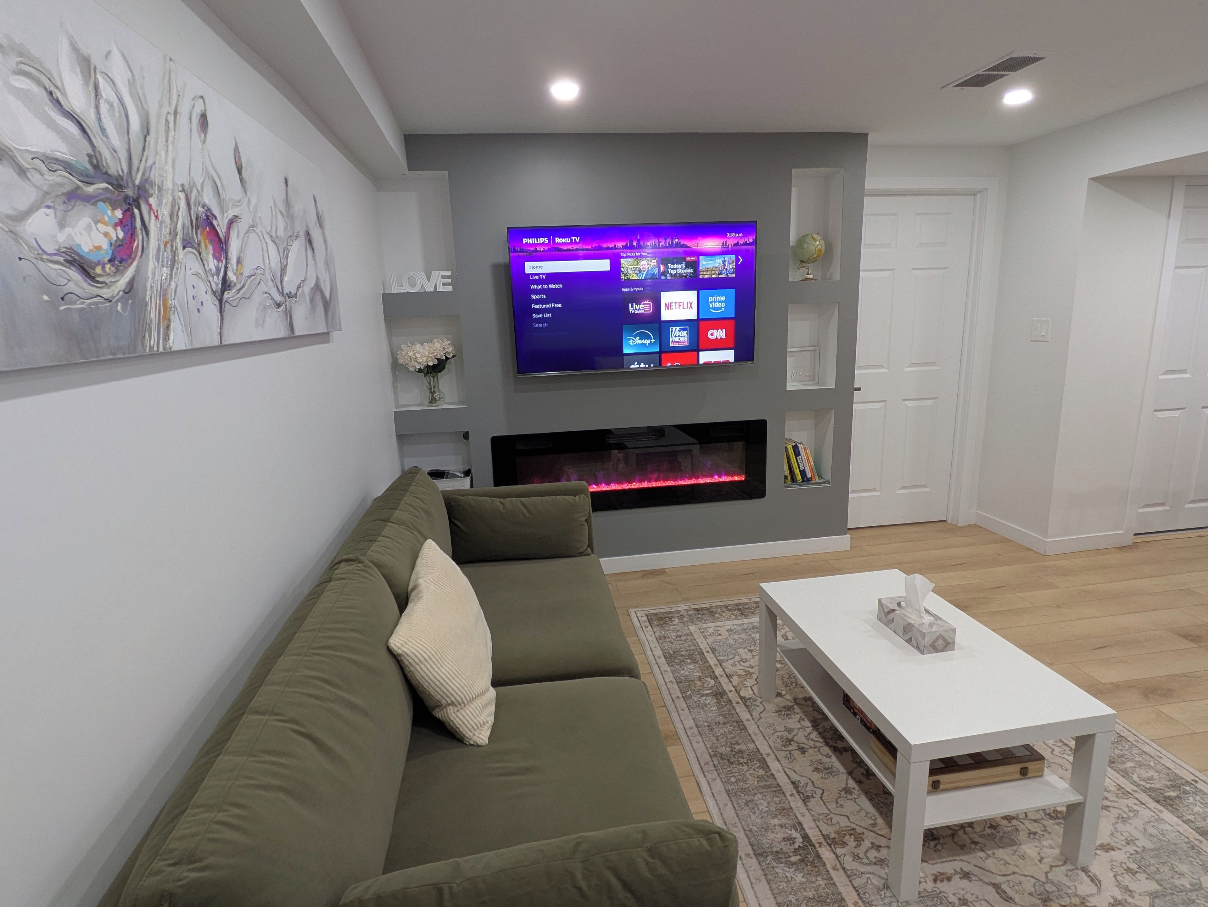 Ein modernes Wohnzimmer mit einem Flachbildfernseher über einem Kamin, einem grünen Sofa und einem weißen Couchtisch.