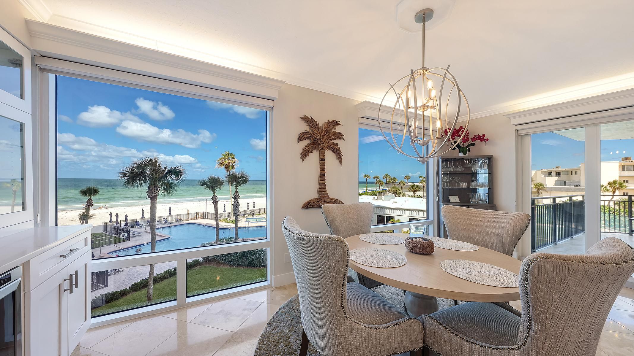 A spacious dining area with a view of the beach and pool, modern furniture, and a decorative palm tree.