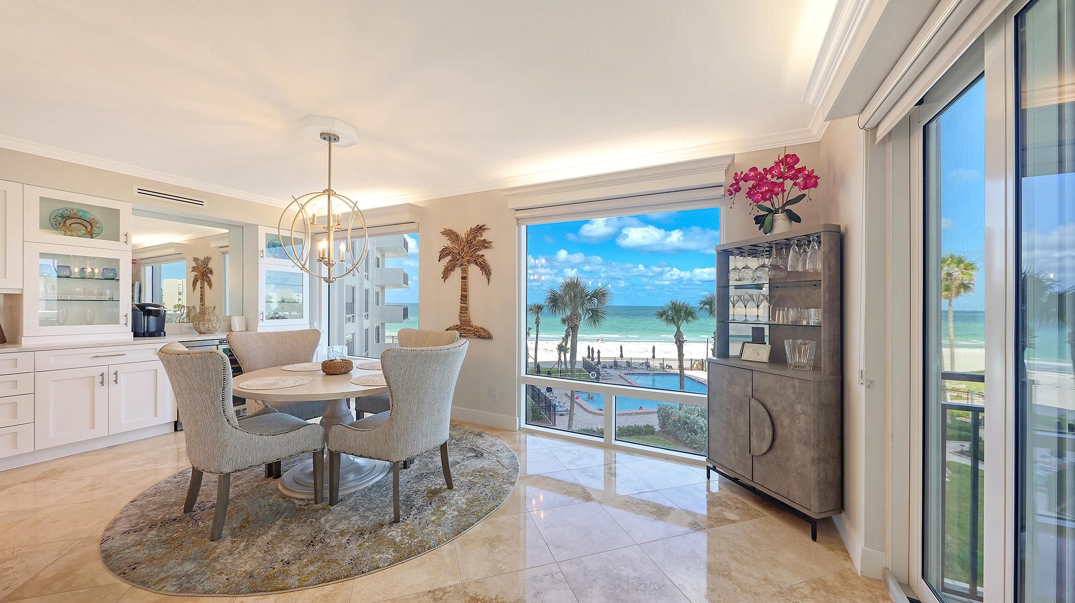 A modern kitchen with a view of the beach, a dining area with a round table, and a bar area with a large window.