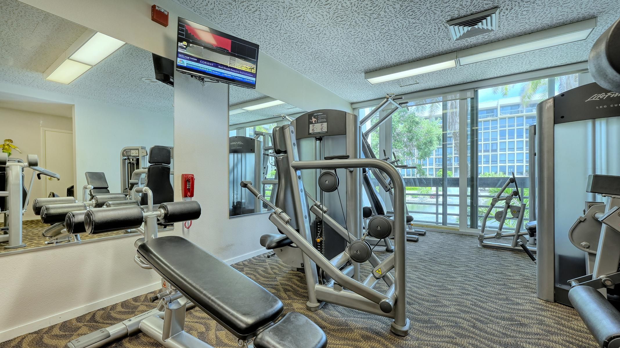 A gym with various exercise equipment, a large mirror, and a television displaying financial data.