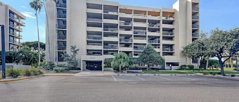 Exterior view of six-story condo building with balconies, surrounding palm trees, and reserved parking spaces.
