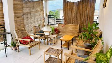 A room with a balcony, bamboo blinds, and various seating arrangements including chairs and a sofa.
