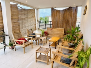 A room with a balcony, bamboo blinds, and various seating arrangements including chairs and a sofa. - Room-beautiful Room With Private Toilet (Bamako)