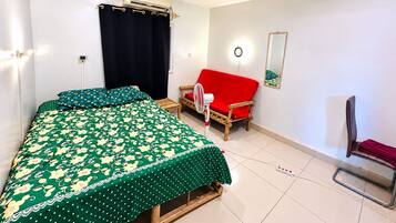 A bedroom with a bed, a red sofa, a chair, an air conditioning unit, and a mirror on the wall.