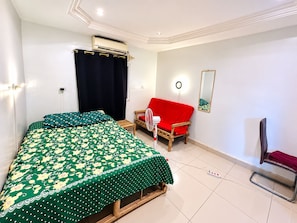 A bedroom with a bed, a red sofa, a chair, an air conditioning unit, and a mirror on the wall. - Room-beautiful Room With Private Toilet (Bamako)