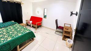 Ett rum med en säng, en röd soffa, en stol, ett litet bord, en tv som hänger på väggen och en dörr.