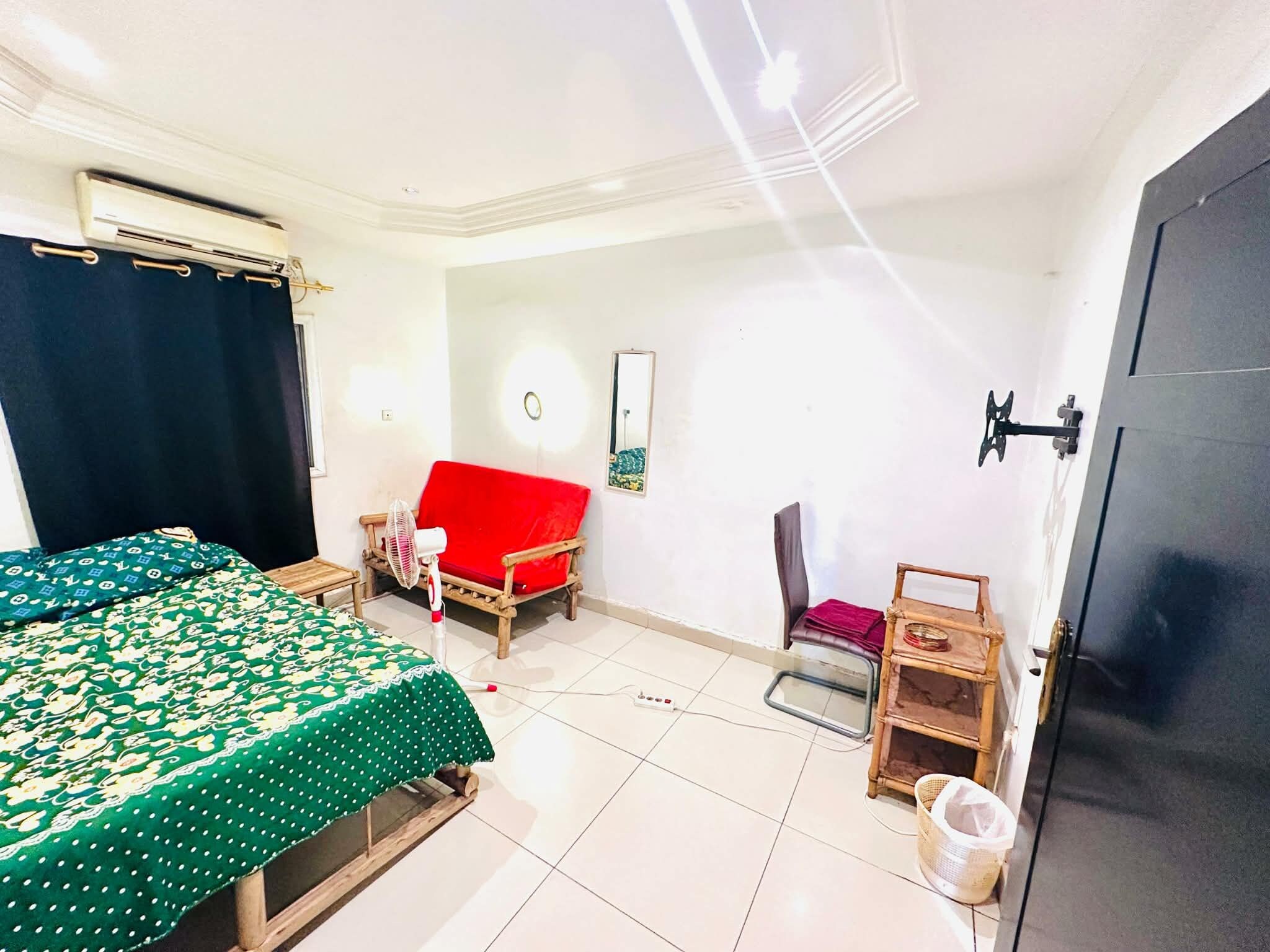 A room with a bed, a red sofa, a chair, a small table, and a trash bin.