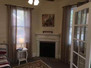 Una habitación con chimenea, un cuadro sobre ella, una mesita con una lámpara y una cama con ropa de cama a rayas.