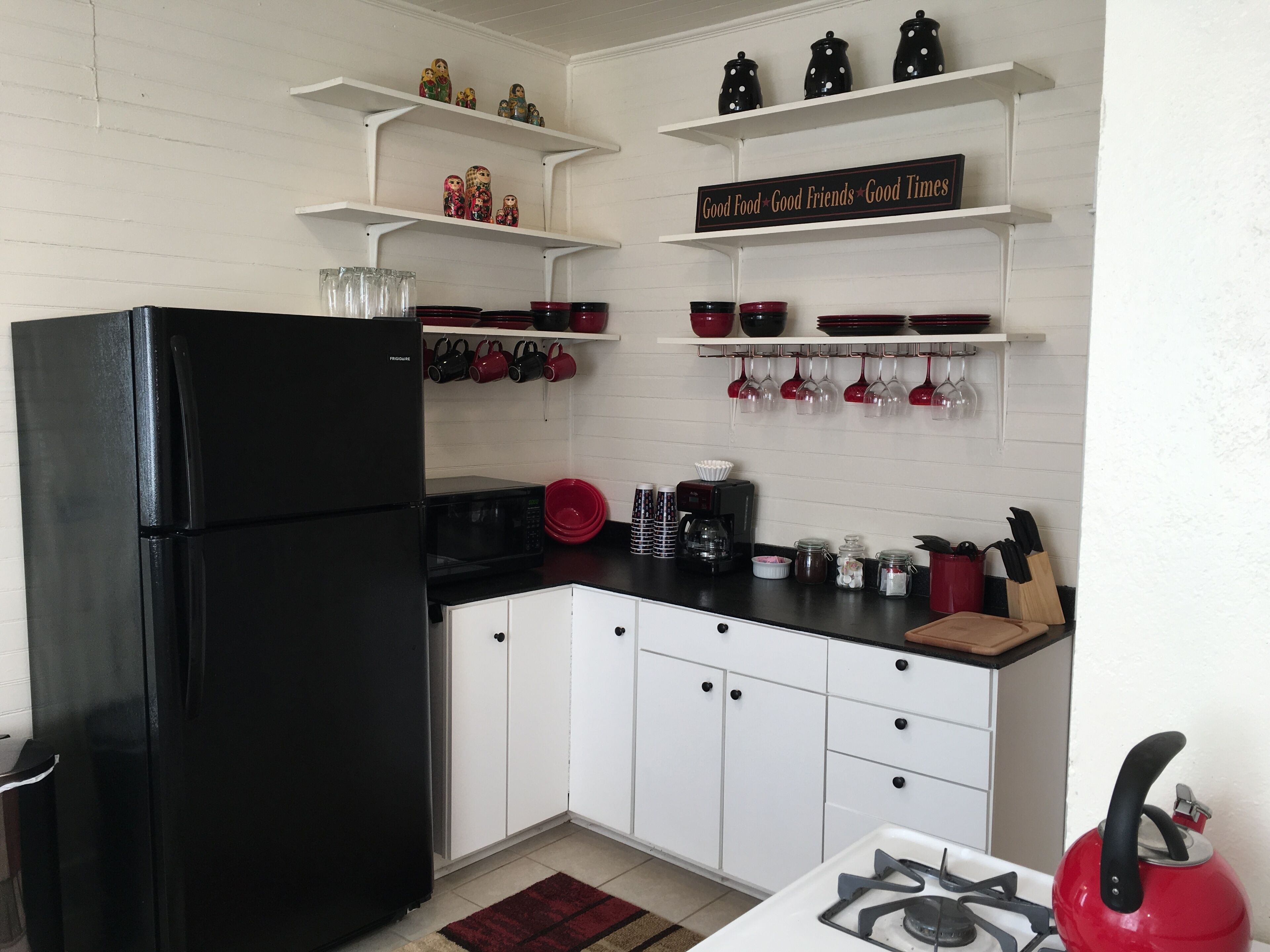 A kitchen with white cabinets, a black refrigerator, a gas stove, and shelves with kitchenware.