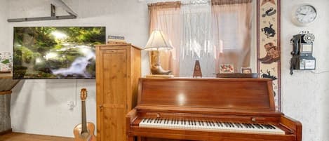 A living room with a wooden piano, a television, a guitar, and a wall clock.