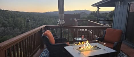 Um deck externo com lareira, móveis de vime e vista para a floresta.