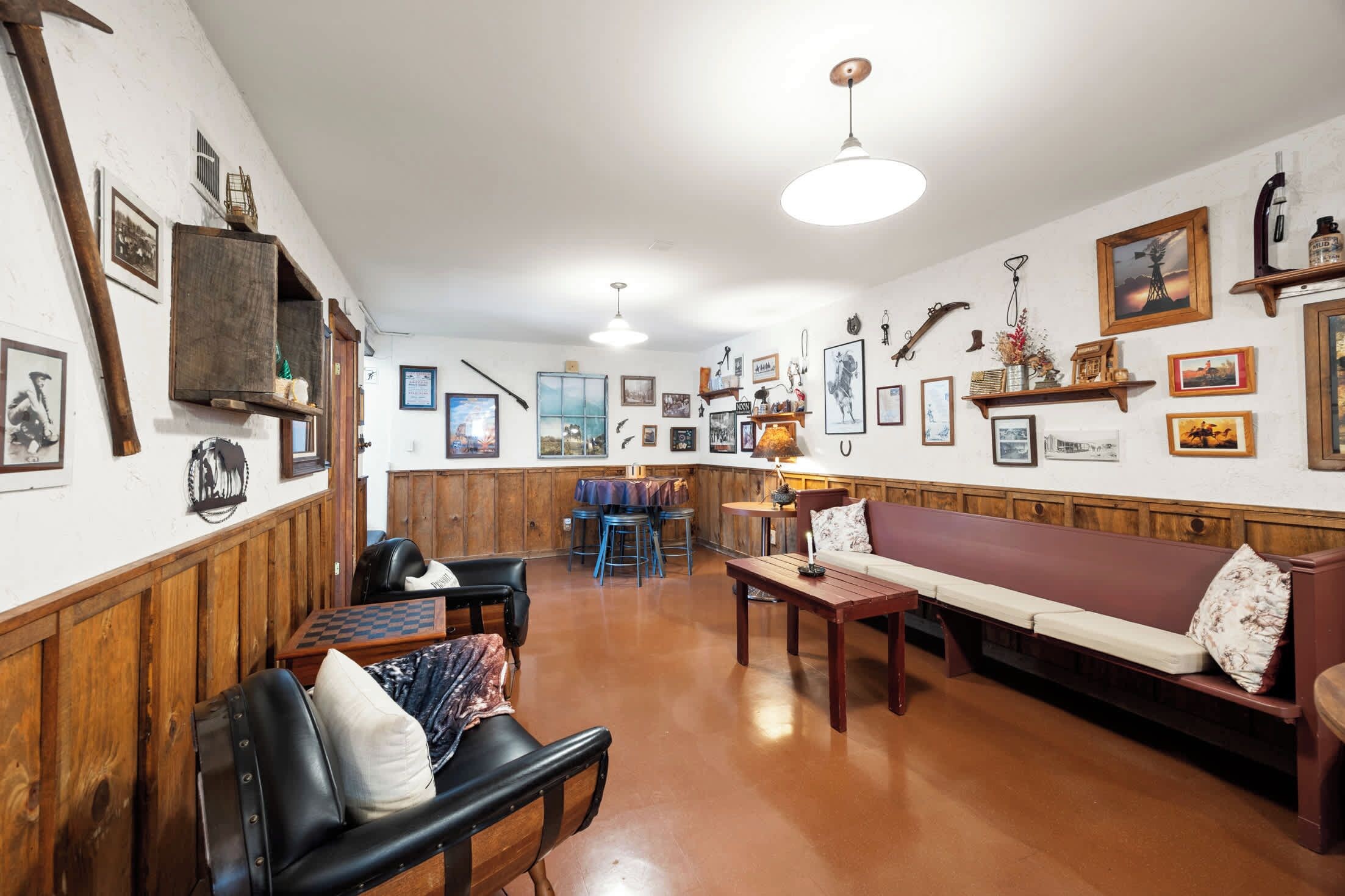 Une pièce chaleureuse avec un banc en bois, une table et un canapé. Les murs sont ornés de tableaux encadrés et le plafond est éclairé par un luminaire.