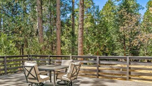 A deck with two chairs and a table, surrounded by a wooden fence, overlooking a forest. - Once Upon A Blue Pine (Idyllwild-Pine Cove)