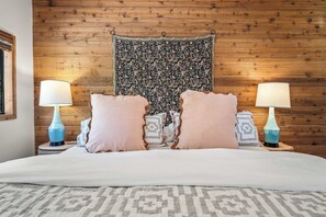 Ein Schlafzimmer mit einem hölzernen Kopfteil, einer gemusterten Wandteppich, zwei Nachttischlampen und einem Bett mit einer gemusterten Bettdecke.