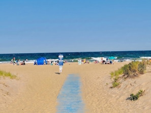 A beach with a clear path leading to the water, people relaxing, and a blue tent.
