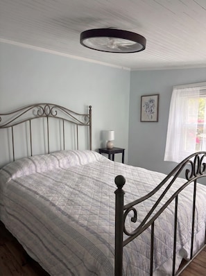 A bedroom with a bed, a bedside table, a lamp, a window with curtains, and a ceiling fan.