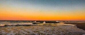 Una playa con olas, un promontorio rocoso y una persona de pie sobre las rocas.