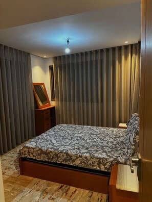 A bedroom with a bed, a nightstand, a mirror, and curtains. - NEW Modern Apartment Heart of Mohammedia (Mohammedia)
