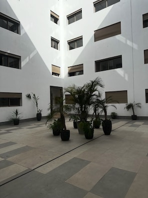 A courtyard with a modern building, potted plants, and a tiled floor. - NEW Modern Apartment Heart of Mohammedia (Mohammedia)