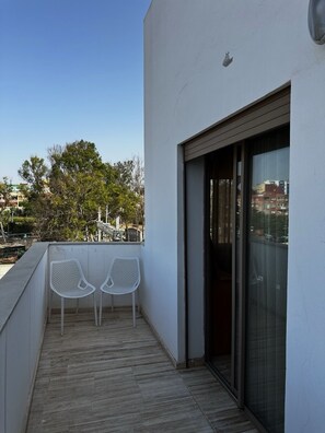A balcony with two white chairs, a wooden floor, and a view of buildings and trees in the background. - NEW Modern Apartment Heart of Mohammedia (Mohammedia)