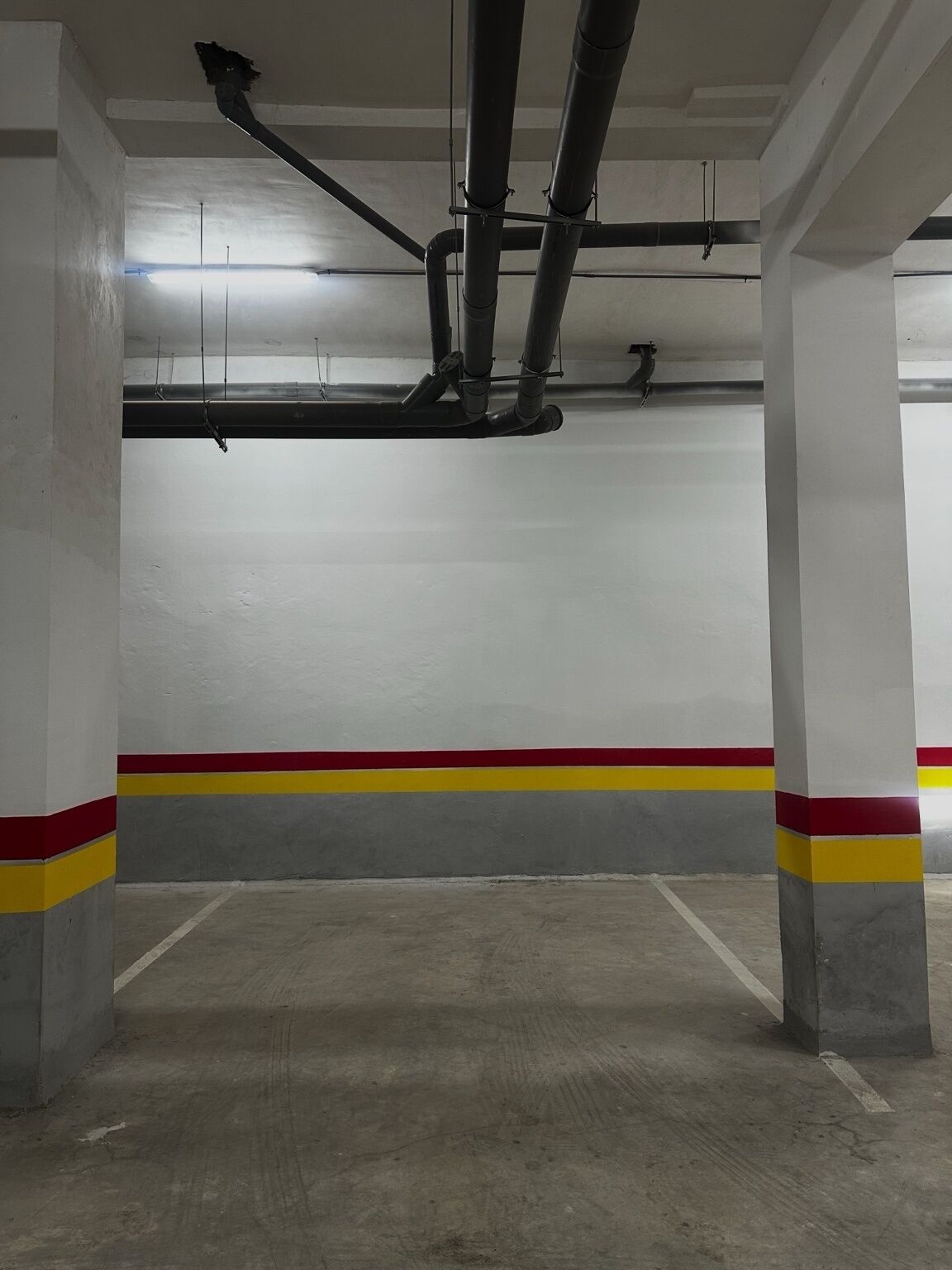 Garagem de estacionamento vazia, com pilares de concreto e faixa amarela e vermelha no chão.