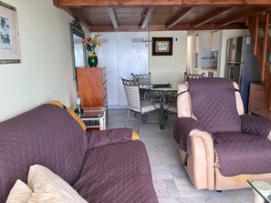 Uma sala de estar aconchegante com duas poltronas reclináveis, uma mesa de jantar com cadeiras, uma cozinha com geladeira e um vaso decorativo com flores.