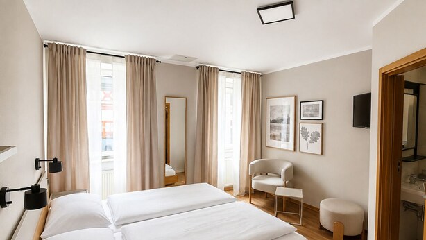 Ein Hotelzimmer mit Bett, Stuhl, kleinem Tisch, Spiegel und Bildern an der Wand.