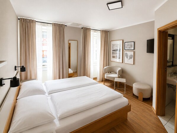 Una camera d'albergo con un letto, una sedia, un tavolino, uno specchio e opere d'arte alle pareti.