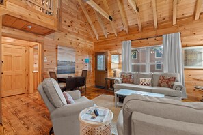 L’intérieur d’un chalet en bois comprend un coin repas, un canapé et une fenêtre avec des rideaux.