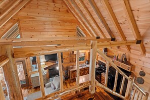 Interior de una cabaña de madera con habitación en el altillo, cocina y sala de estar.