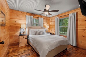 A wooden cabin bedroom with a bed, nightstands, a ceiling fan, and a window with curtains. - Fancy's Find homey cabin with breathtaking vistas! (Mentone)