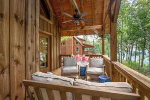 Une terrasse en bois avec une table et des chaises, d’où l’on a vue sur un chalet et une forêt.