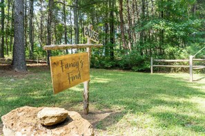 Un panneau indicateur en bois, sur lequel on peut lire « Fancy’s Find », est placé dans une zone boisée. Au premier plan, on aperçoit de l’herbe, et au fond, une clôture en bois.