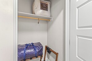 Ein Schrank mit einer Ablage, auf der sich eine Tasche Avocado Dream Better Down Matratzenauflage und eine blaue Tasche auf einem Stuhl befinden.