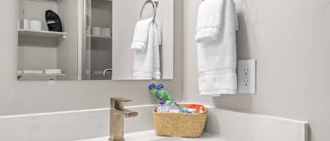 A bathroom with a white sink, a mirror, and two white towels hanging on hooks.