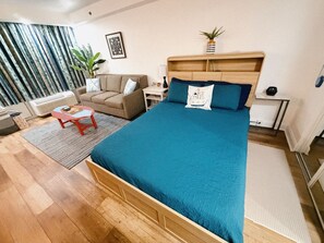 Quarto com cama, sofá, mesinha, planta e janela com cortinas.