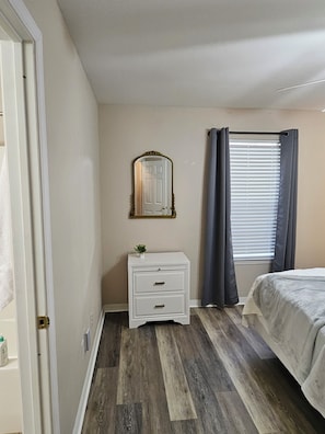 A bedroom with a bed, a nightstand with drawers, a mirror, and a window with curtains. - Gameday Guesthouse 2BR/2BA updated townhome in fabulous Starkville 5 min to MSU (Starkville)