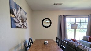 A dining area with a wooden table, chairs, a clock, and a painting on the wall. - Gameday Guesthouse 2BR/2BA updated townhome in fabulous Starkville 5 min to MSU (Starkville)