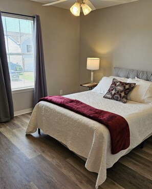 A bedroom with a bed, a nightstand, a lamp, and a window with curtains. - Gameday Guesthouse 2BR/2BA updated townhome in fabulous Starkville 5 min to MSU (Starkville)