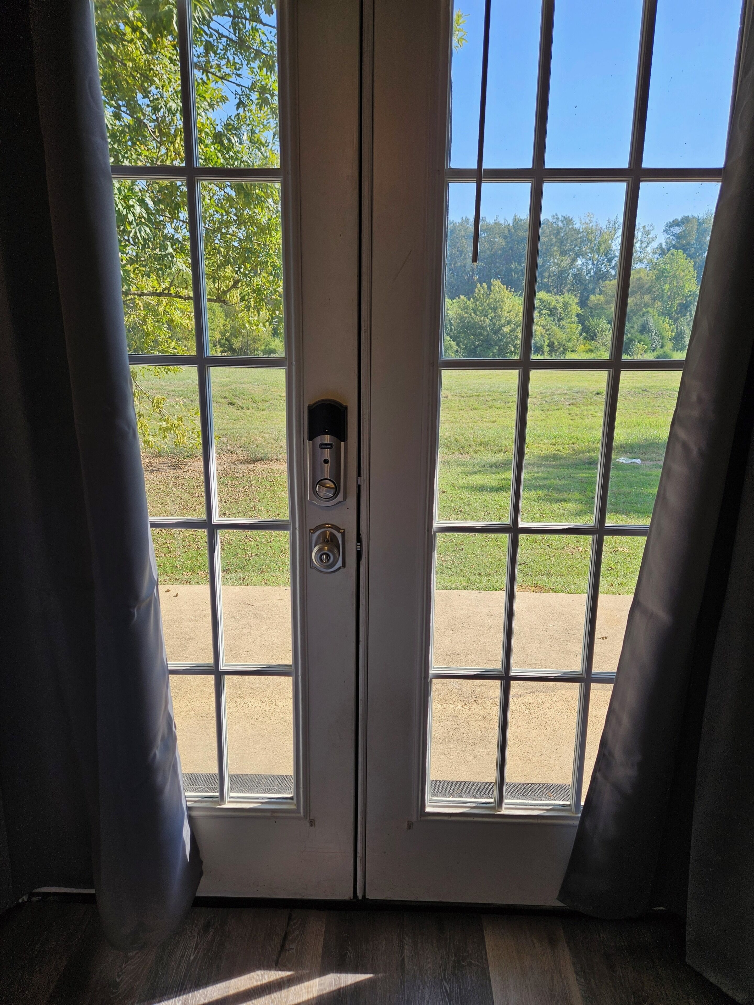 A door with a keypad lock and a view of a grassy field through the window.