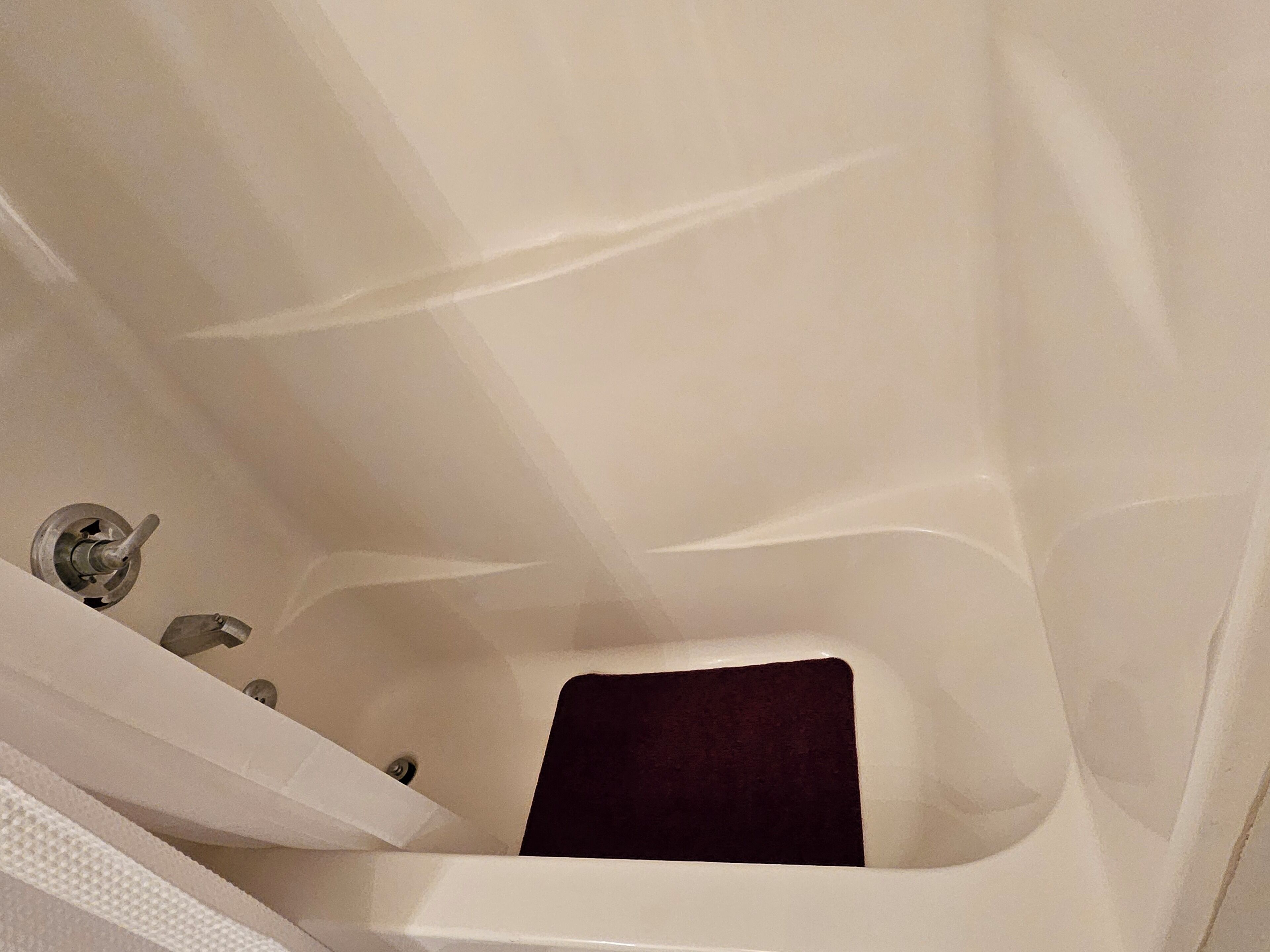 A bathtub with a dark-colored mat, a faucet, and a showerhead.