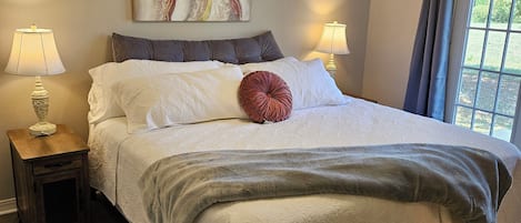 A bedroom with a bed, two bedside lamps, a ceiling fan, and a window with curtains.