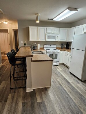 A modern kitchen with white cabinetry, a central island, a microwave, stove, and a refrigerator. - Gameday Guesthouse 2BR/2BA updated townhome in fabulous Starkville 5 min to MSU (Starkville)