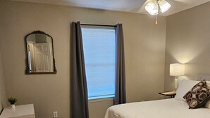 A bedroom with a bed, a nightstand, a lamp, a ceiling fan, a window with curtains, and a mirror on the wall. - Gameday Guesthouse 2BR/2BA updated townhome in fabulous Starkville 5 min to MSU (Starkville)