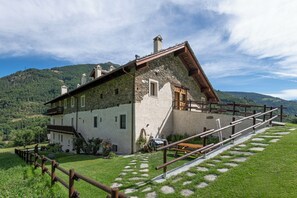 Ein Steinhaus mit einem geneigten Dach, einem hölzernen Balkon und einer Treppe zu einer Holzterrasse.